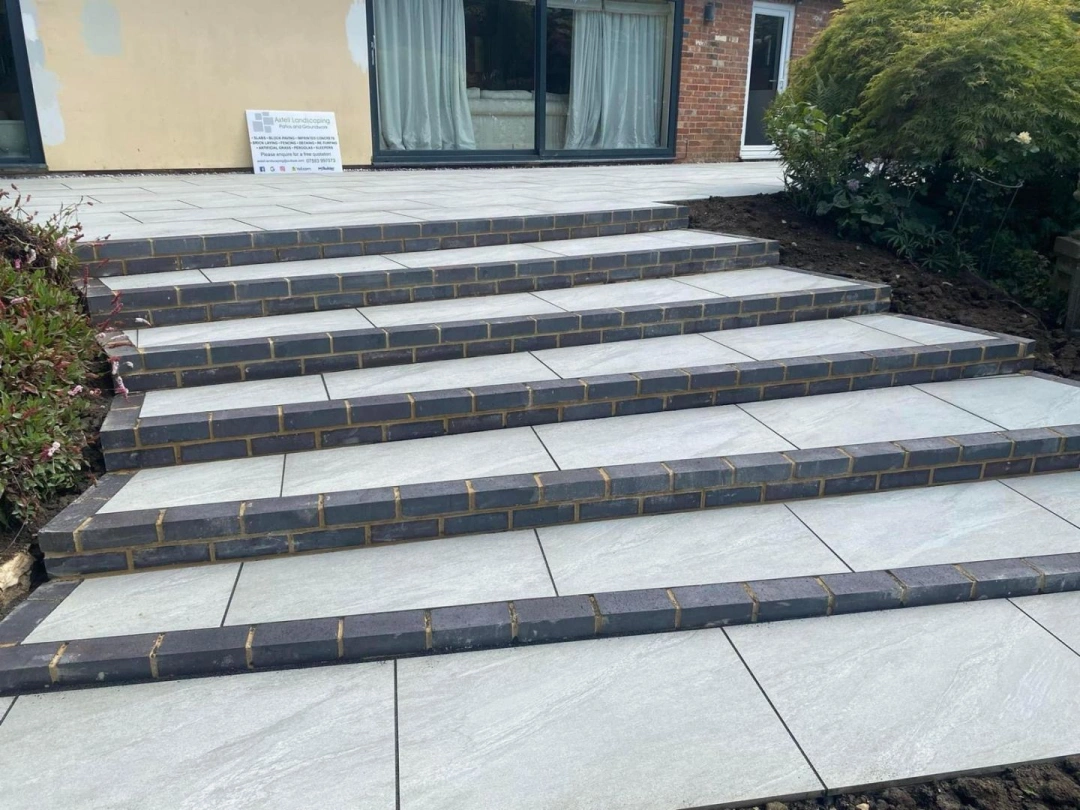 Wide tiled patio steps with dark brick edging by Axtell Landscaping
